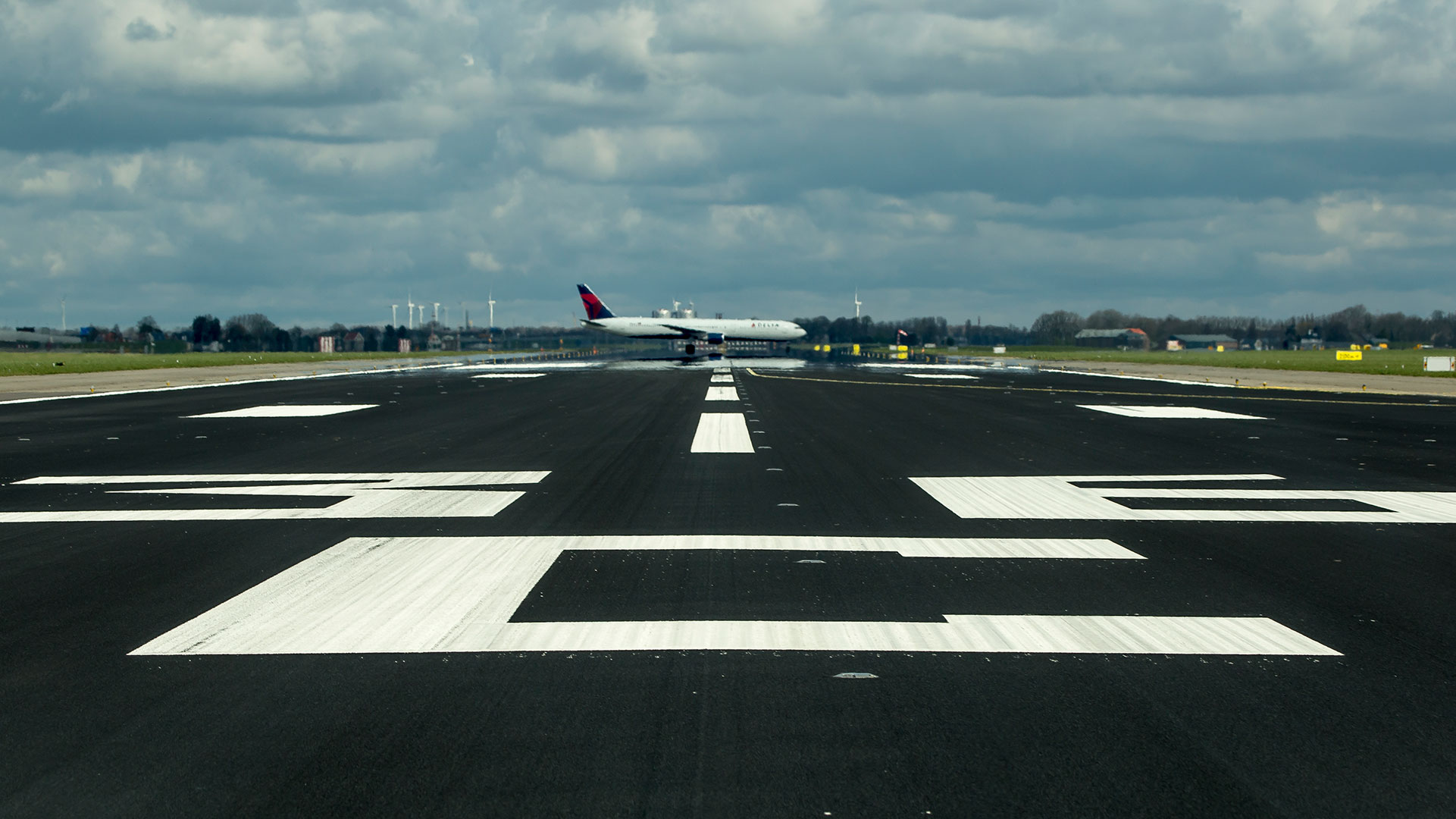 Airport runway maintenance operations with aircraft taxiing at Schiphol Airport.